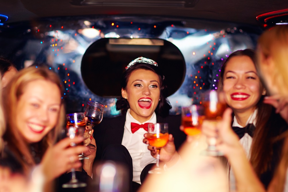 group of happy elegant women clinking glasses in limousine, hen party